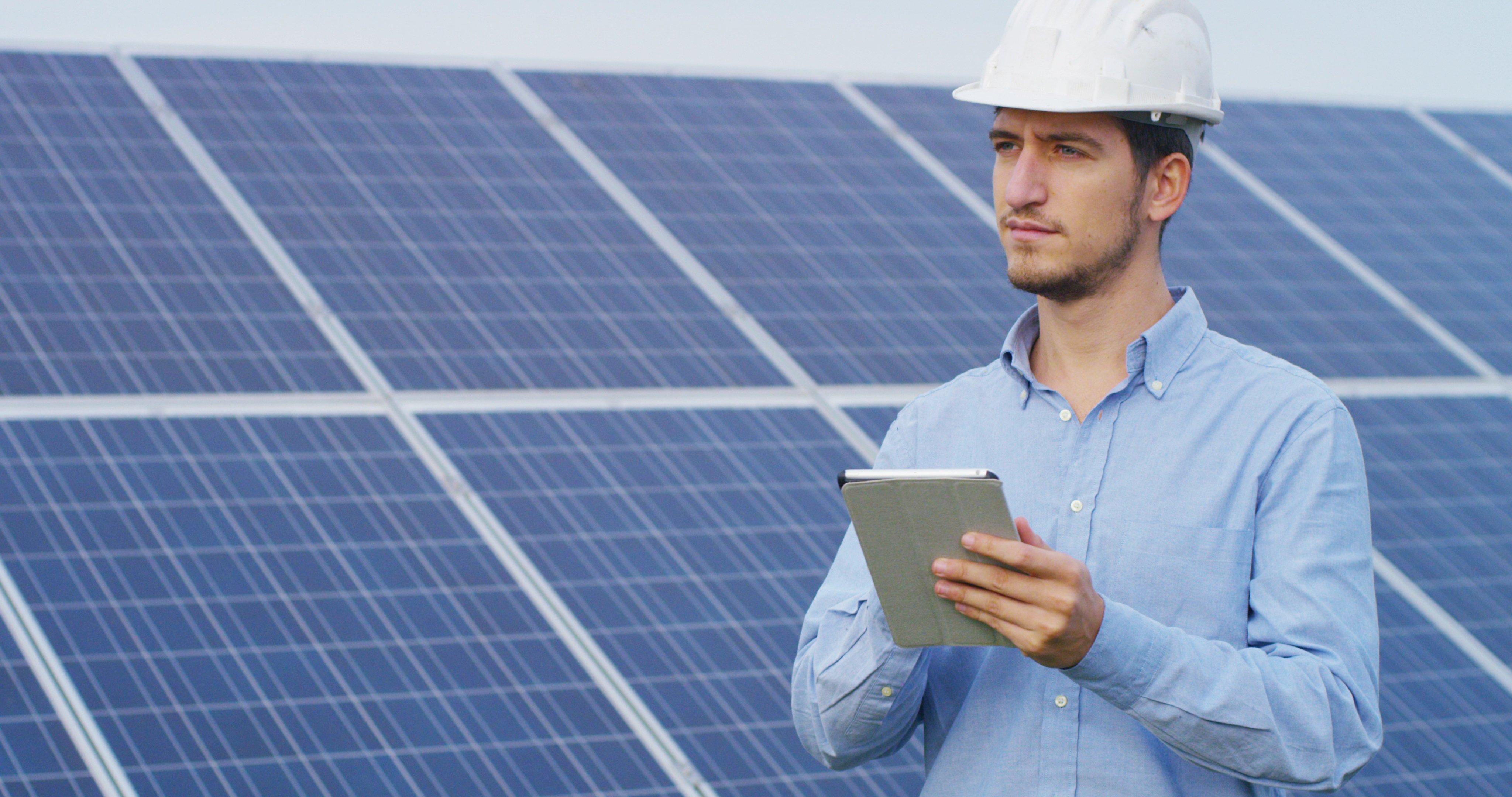 Field Service Engineer with tablet and hard hat beside solar panels